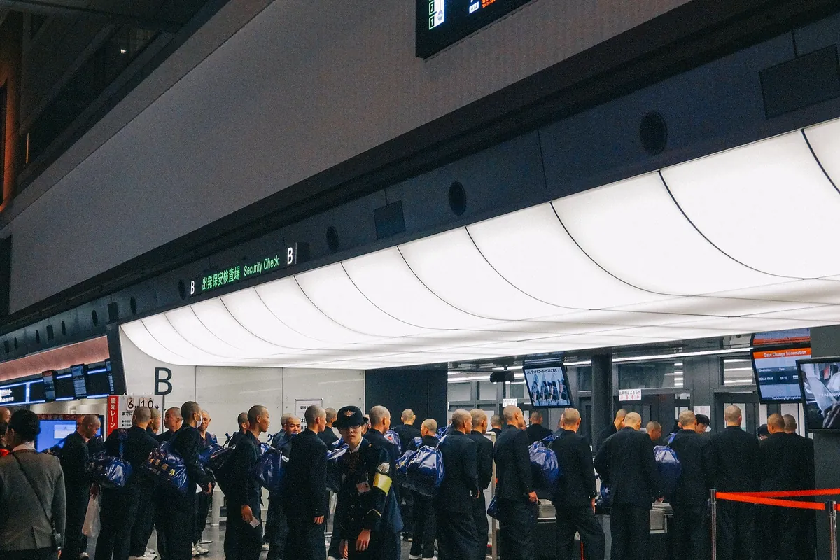 A group of people lined up at an airport security checkpoint under a sign reading Security Check