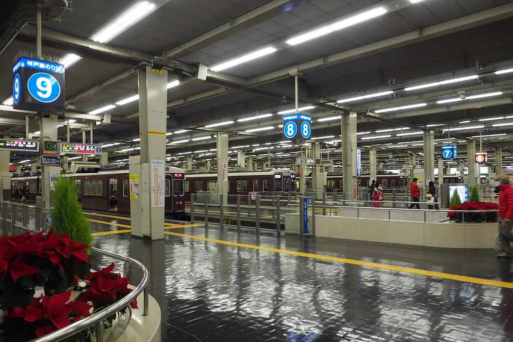 Maroon Hankyu trains at the platforms of Osaka-umeda Station, with red poinsettias in the foreground