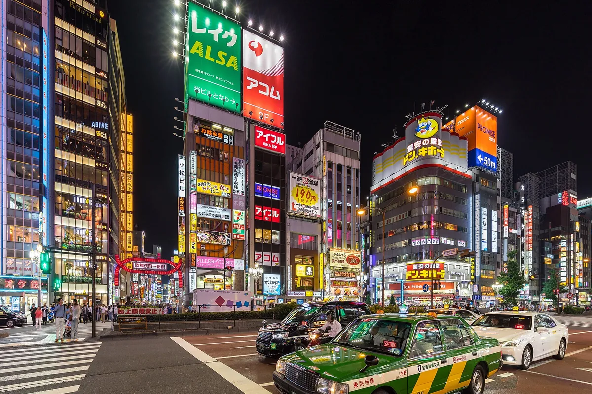 東京・新宿のカラフルなネオンサインの下、夜の靖国通りを走るタクシーと車