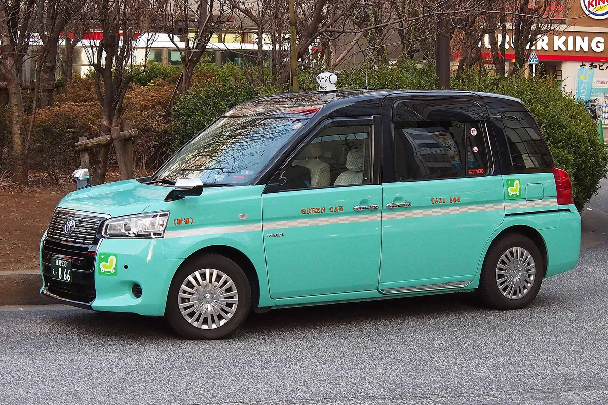 ミントグリーンのGreen CabのトヨタJPN TAXIが、裸の木とバーガーキングの看板がある通りに停まっている
