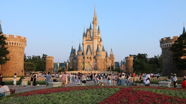 Cinderella Castle at Tokyo Disneyland seen beyond a red and green flower bed, with crowds in the plaza