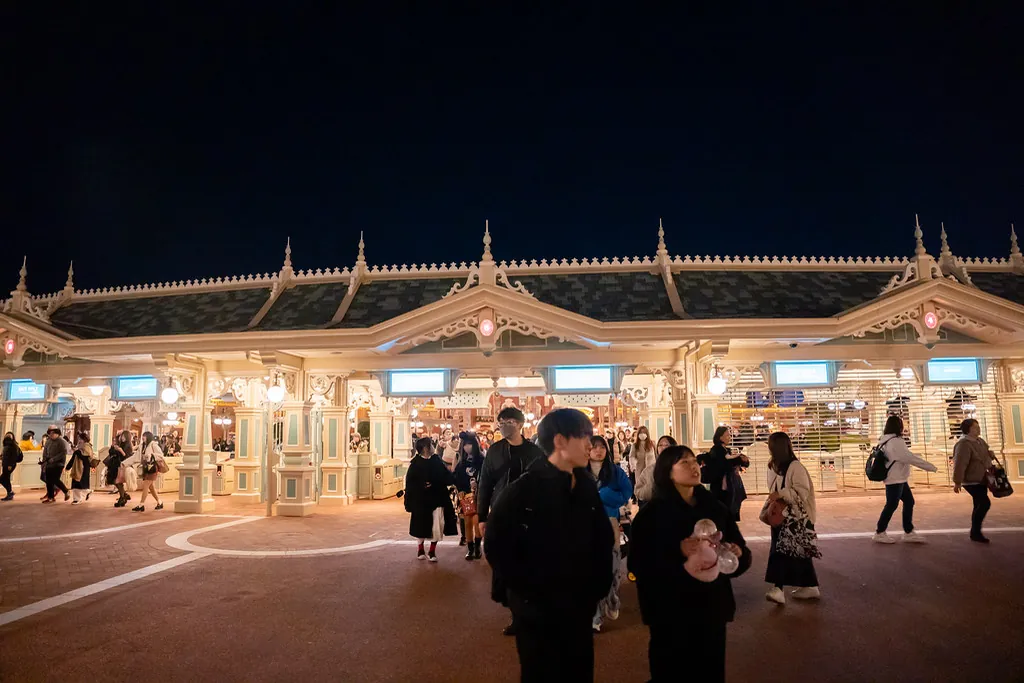 Guests walking past the entrance gate building at Tokyo Disneyland at night