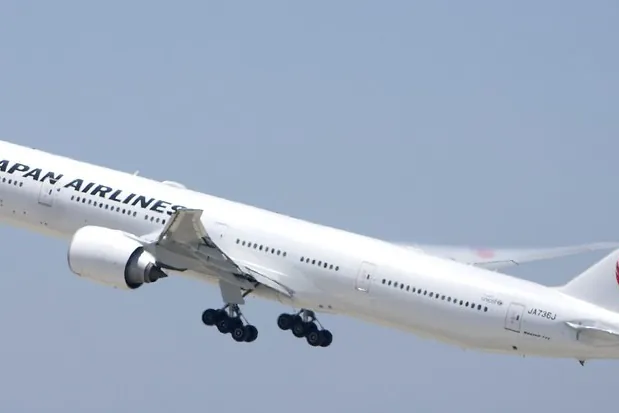 A Japan Airlines Boeing 777 with crane logo on tail climbing after takeoff with landing gear extended