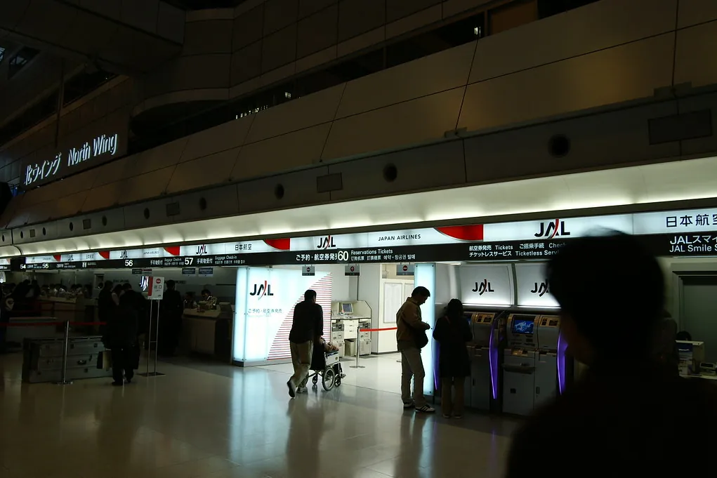 JAL ticket counter with kiosks and airline signage in a dim airport terminal, with passengers nearby