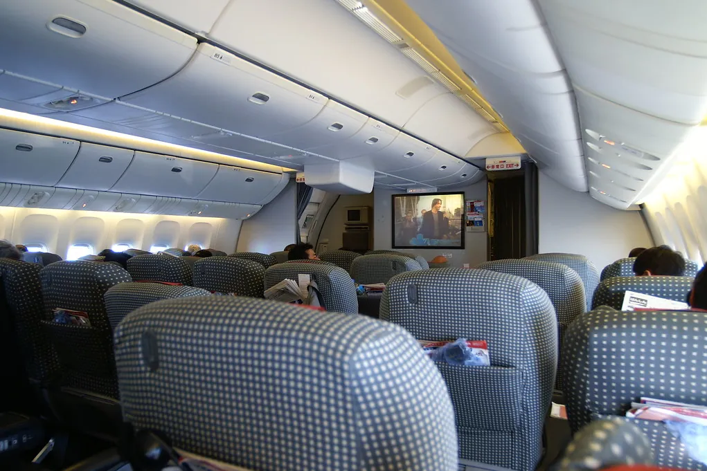 Rows of blue patterned seats inside a JAL aircraft cabin with a screen showing a movie at the front