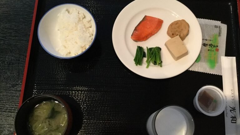 Japanese breakfast on a black tray with a bowl of rice, miso soup, grilled salmon and small side dishes