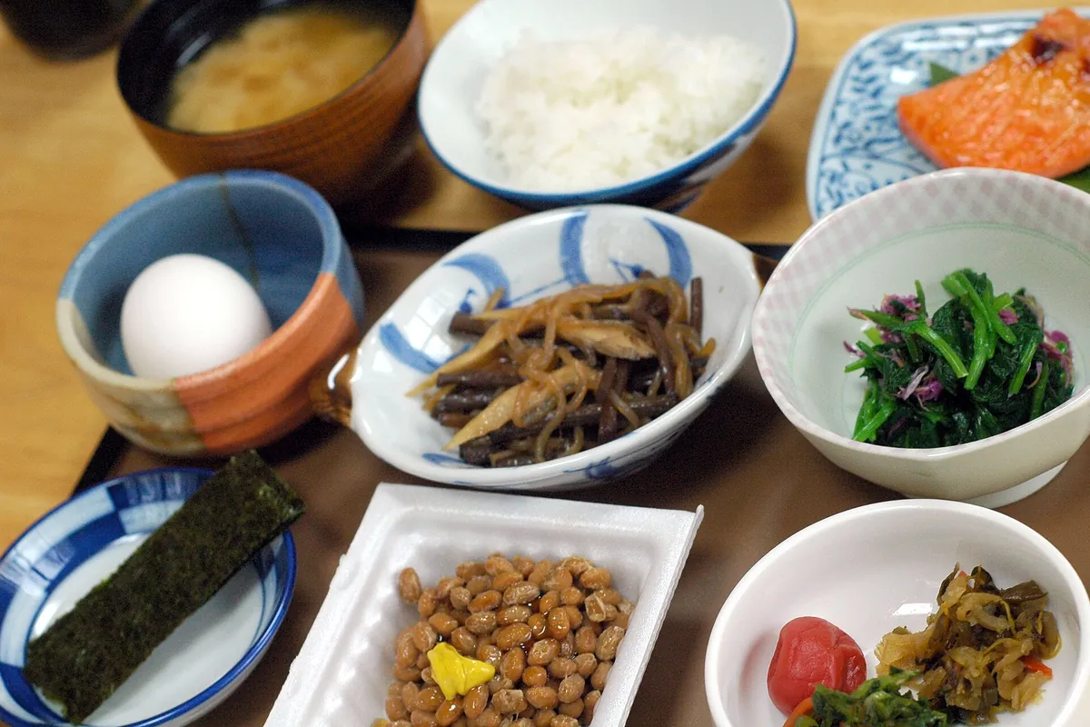 Japanese breakfast with rice, miso soup, grilled salmon, natto, an egg in a cup and pickles in small dishes