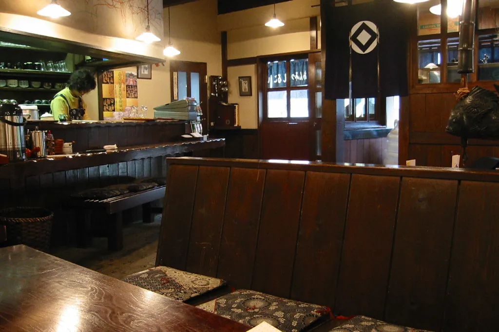 Dark wooden counter and booth seats with patterned cushions in an old-style coffee shop with a noren curtain