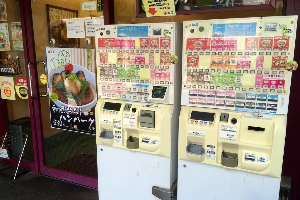 Two meal ticket machines with rows of colorful buttons beside the entrance of a Japanese restaurant