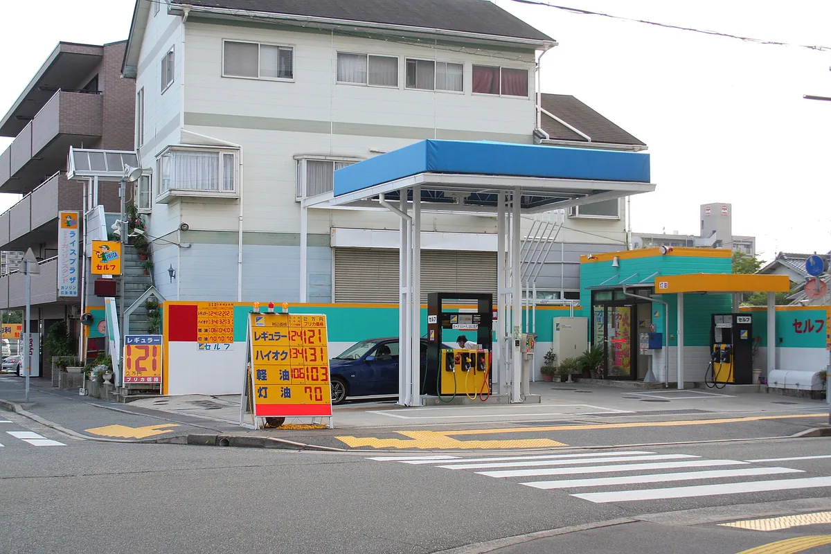 日本的自助加油站，蓝色顶棚下有加油机和价格牌，一辆车正在加油