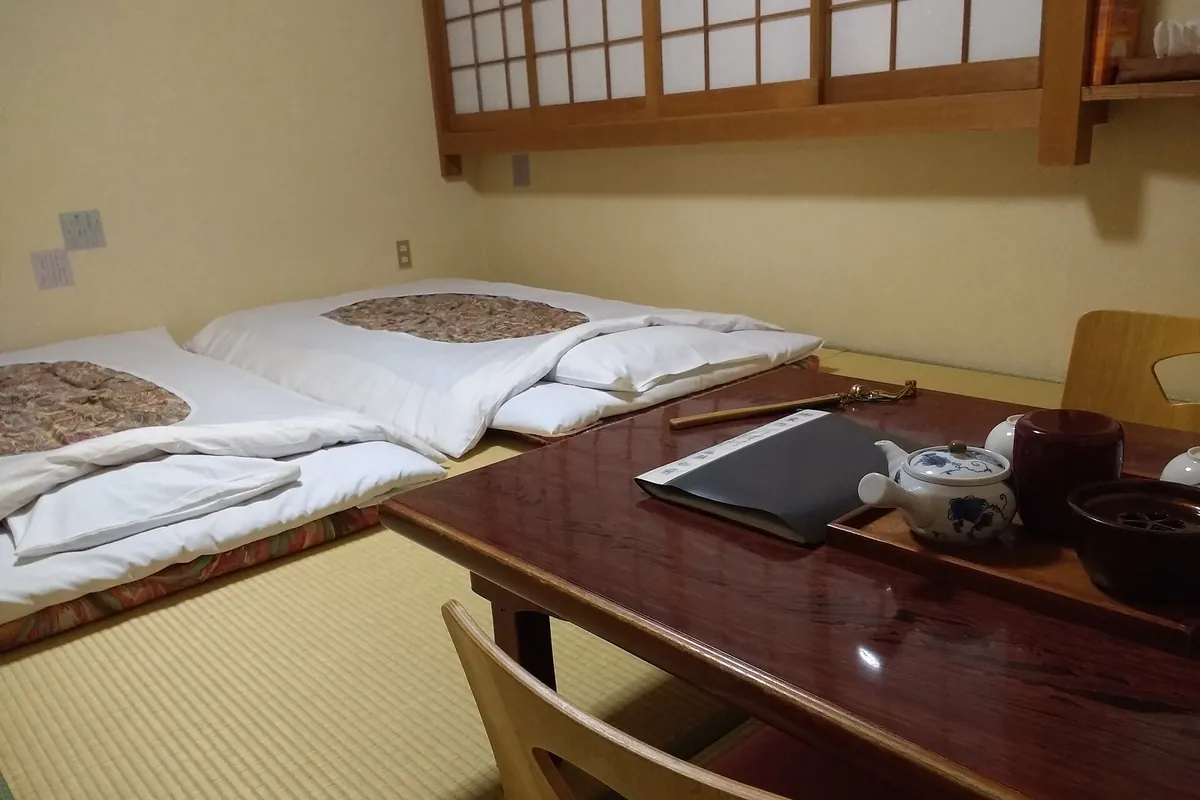 Japanese ryokan room with tatami mats, two futon beds, and a low table with tea set