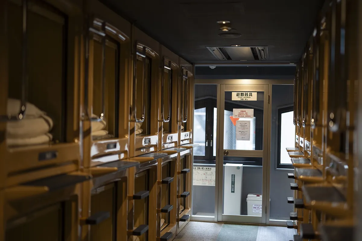 Rows of stacked capsule pods lining a narrow corridor in a Japanese capsule hotel