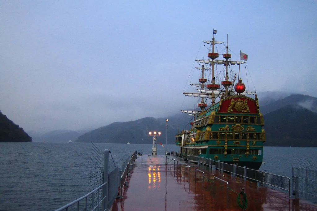 Green galleon-style ship with gold ornaments docked at a pier on Lake Ashi, with hills around the lake