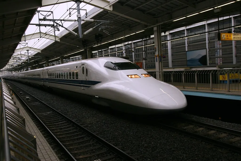 A white Shinkansen bullet train with a blue stripe arriving at a covered station platform in Japan