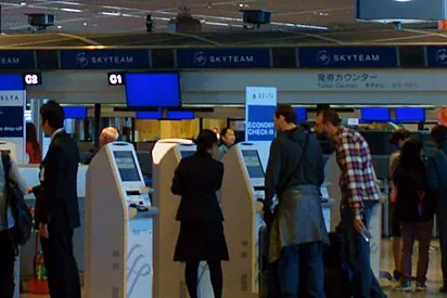 Travellers using self-service check-in kiosks and queuing at airline counters in a Narita Airport departure lobby