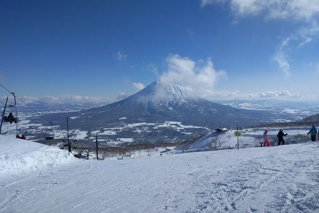 A chairlift and skiers on a snowy slope at a Niseko resort, with snow-capped Mount Yotei in the background