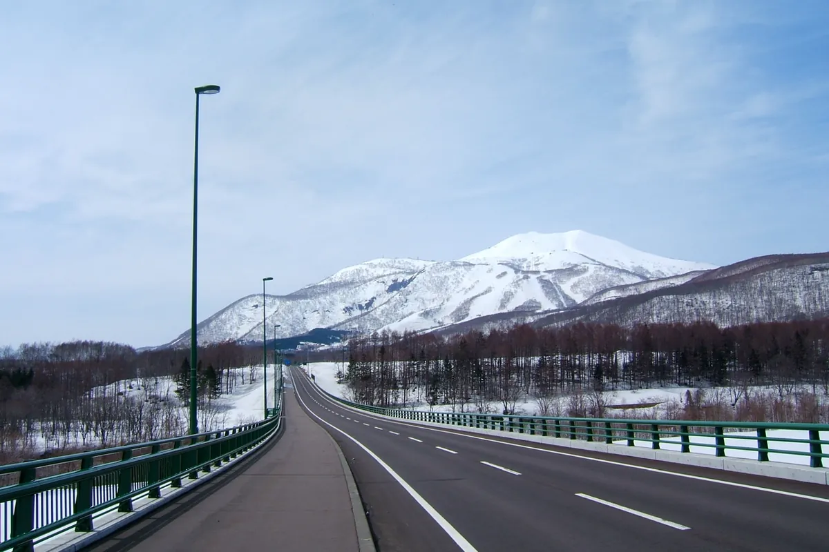 A road and bridge leading toward Niseko Annupuri, its snow-covered slopes marked with ski trails