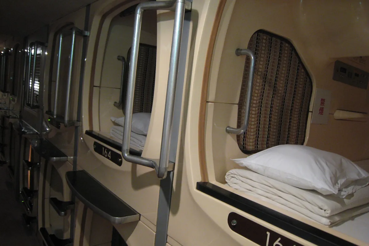 Rows of capsule pods in an Osaka capsule hotel, with open doors showing folded bedding and pillows inside
