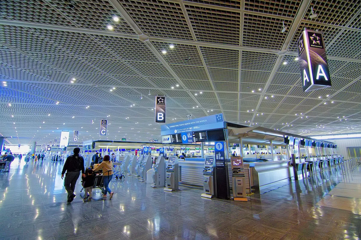 Travellers with luggage walking past airline check-in counters in the departure lobby at Narita Airport, Japan