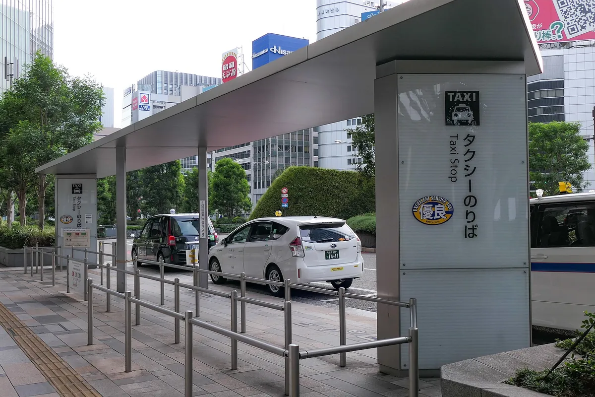 Taxis waiting at a covered taxi stand with a Taxi Stop sign outside an exit of Tokyo Station.