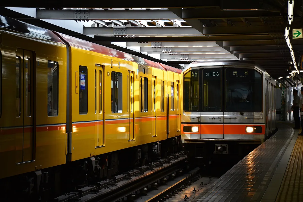 A yellow Tokyo Metro Ginza Line train beside a silver Shibuya-bound train at a covered station platform in Tokyo