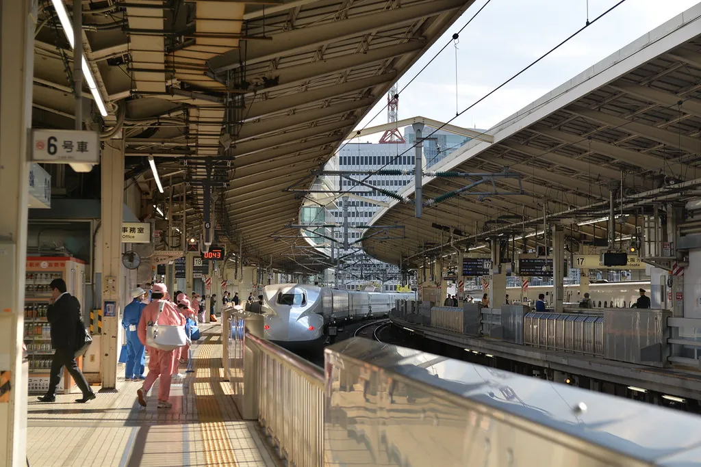 A white Shinkansen train at a curved platform in Tokyo Station with a car number sign overhead