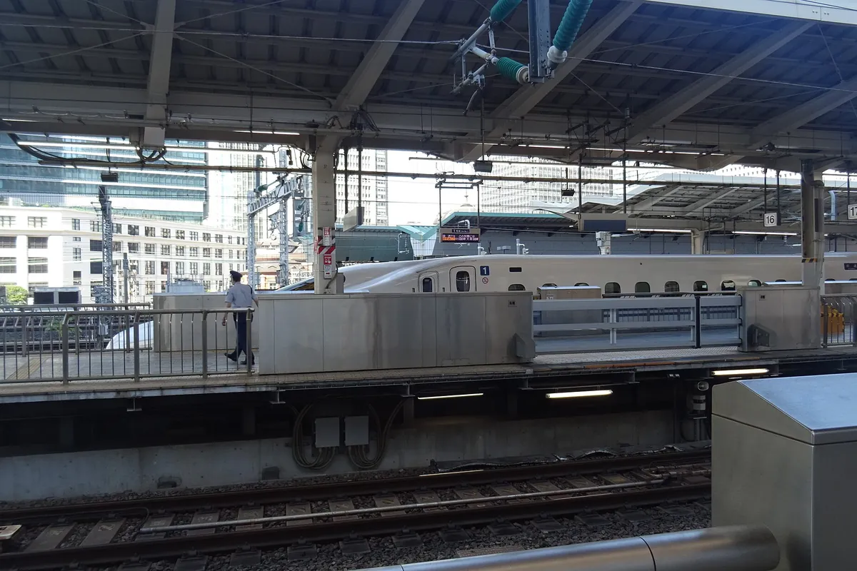 A Shinkansen train at a platform in Tokyo Station with city buildings and a staff member visible