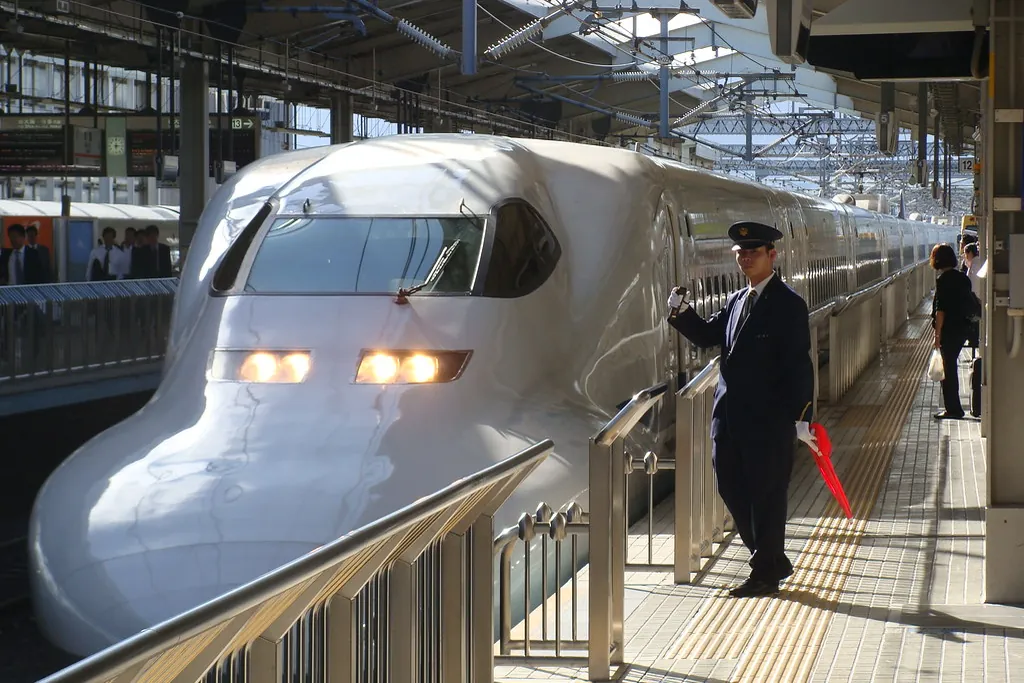 A shinkansen train stopped at a platform with a conductor and passengers waiting beside it