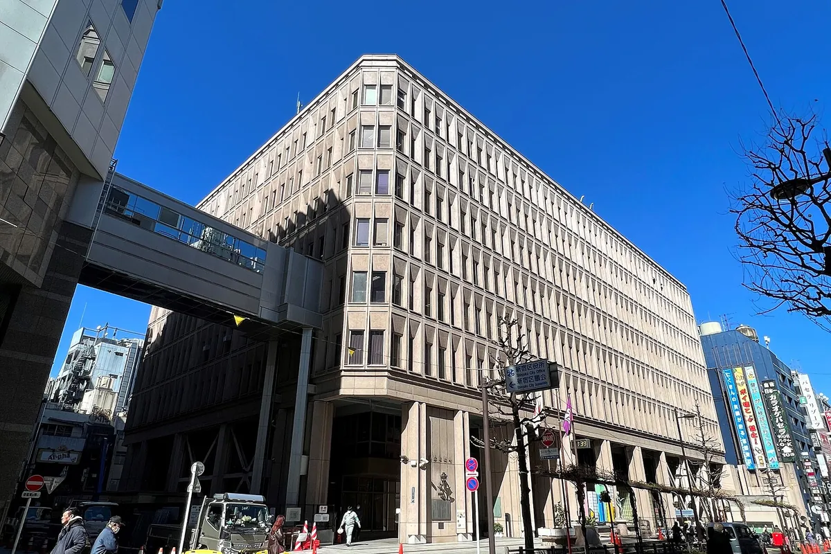 东京新宿区役所大楼外观，有高架步道，街上有行人