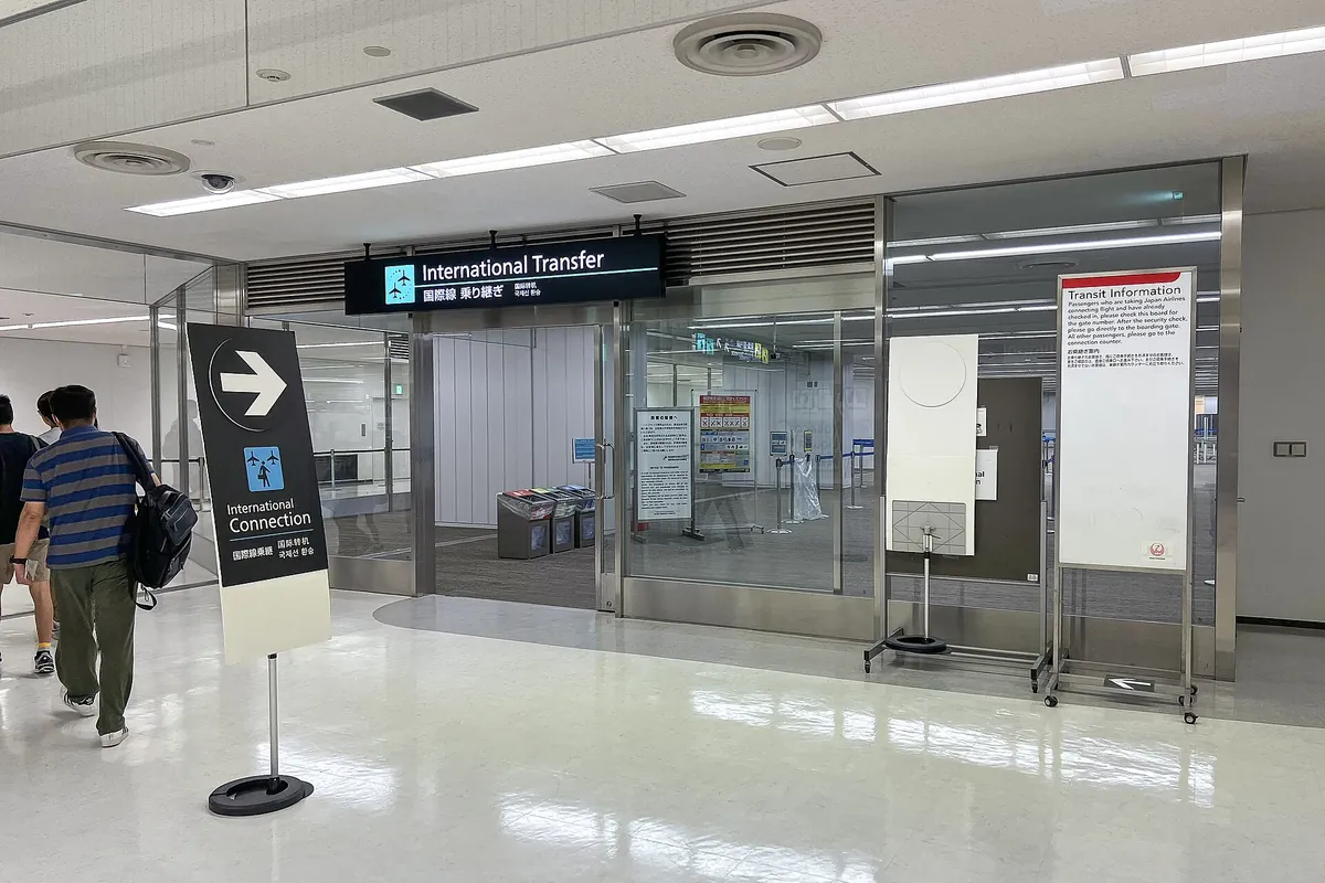 成田机场航站楼内的国际转机指示牌和转机信息板，两名旅客走过