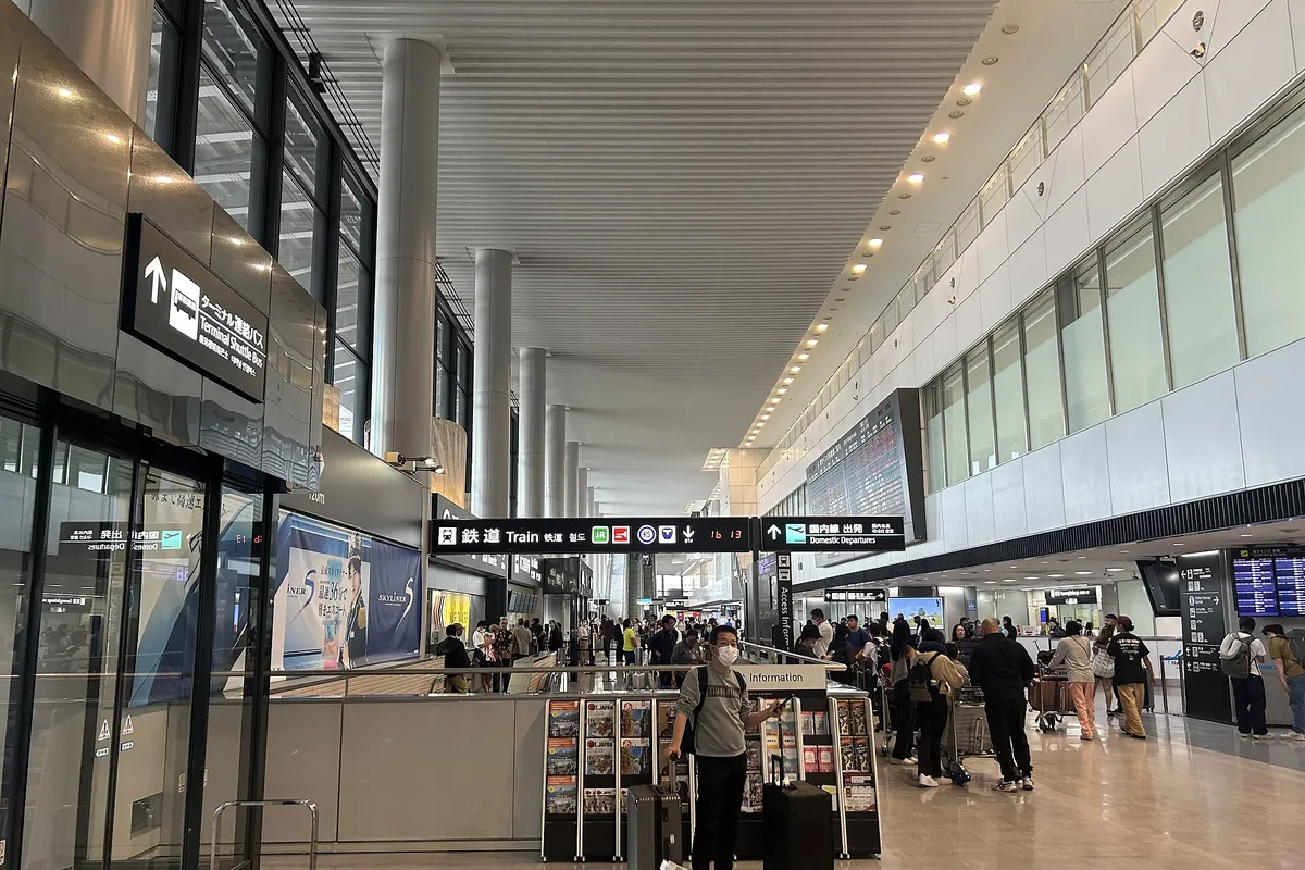 Crowded arrival hall at Narita International Airport Terminal 1 with travelers and luggage near train and departure signs