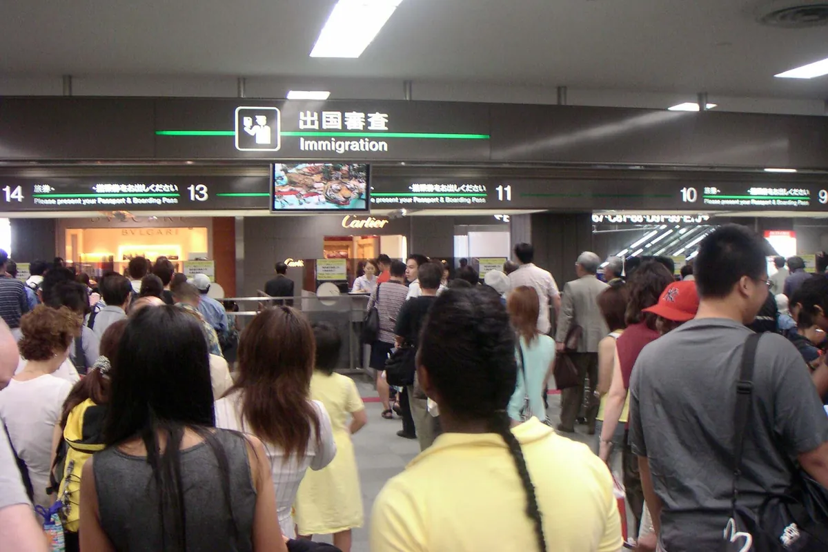Travelers queuing beneath an Immigration sign inside Narita Airport Terminal 2 in Japan