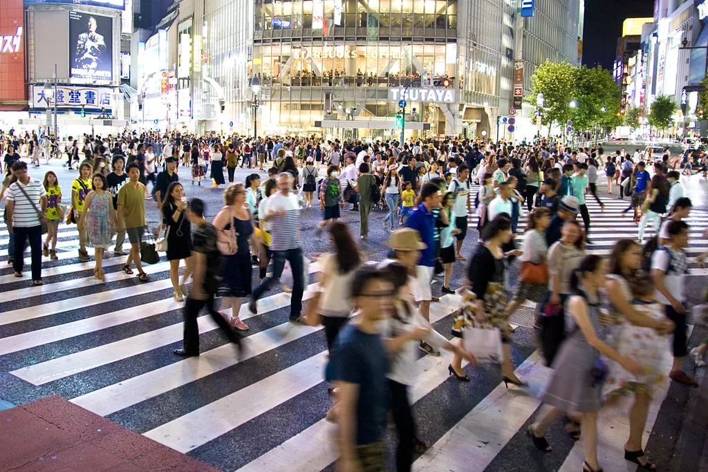 Pedestrians crossing the Shibuya scramble crossing in Tokyo at night with illuminated storefronts and signs