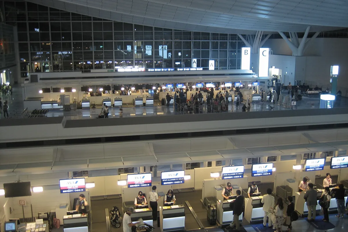 Airline check-in counters on two levels at Haneda Airport at night, with staff and passengers at the lower-level desks