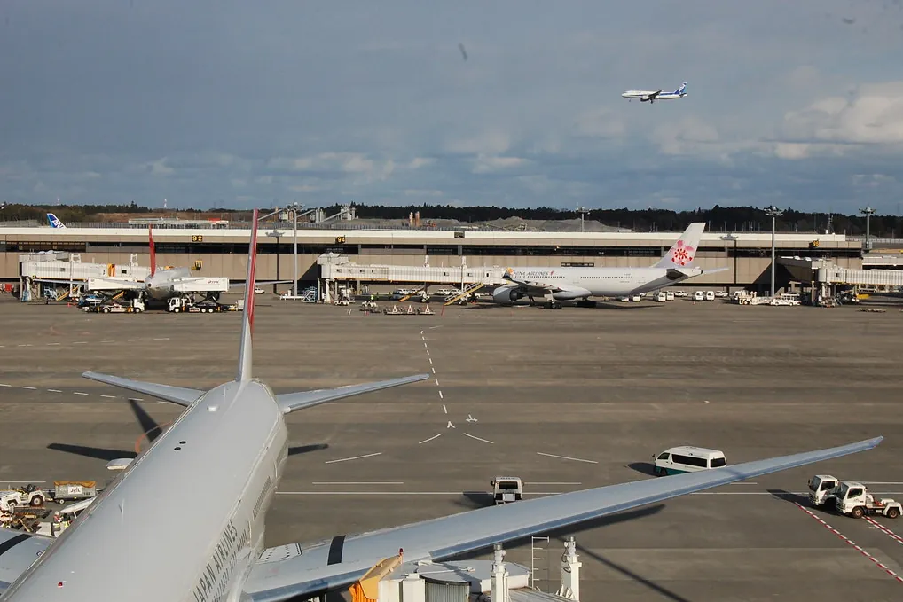 Aircraft parked at gates with another plane flying overhead at Narita Airport Terminal 2
