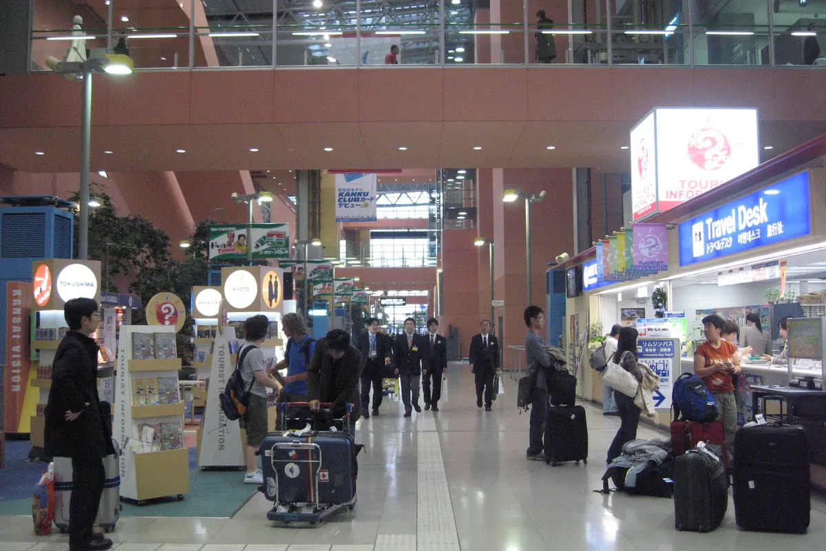 Arrival hall at Kansai International Airport with travellers, luggage carts, and a Travel Desk counter