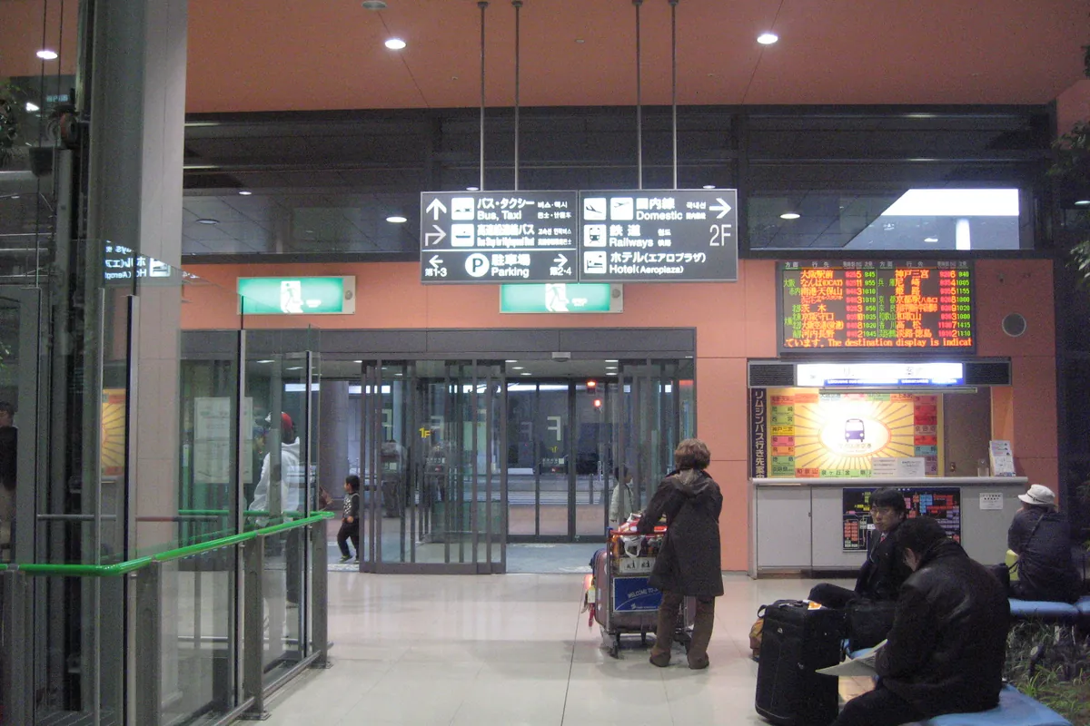 안내판과 승차권 카운터, 짐을 든 여행자들이 있는 간사이 국제공항 도착 로비
