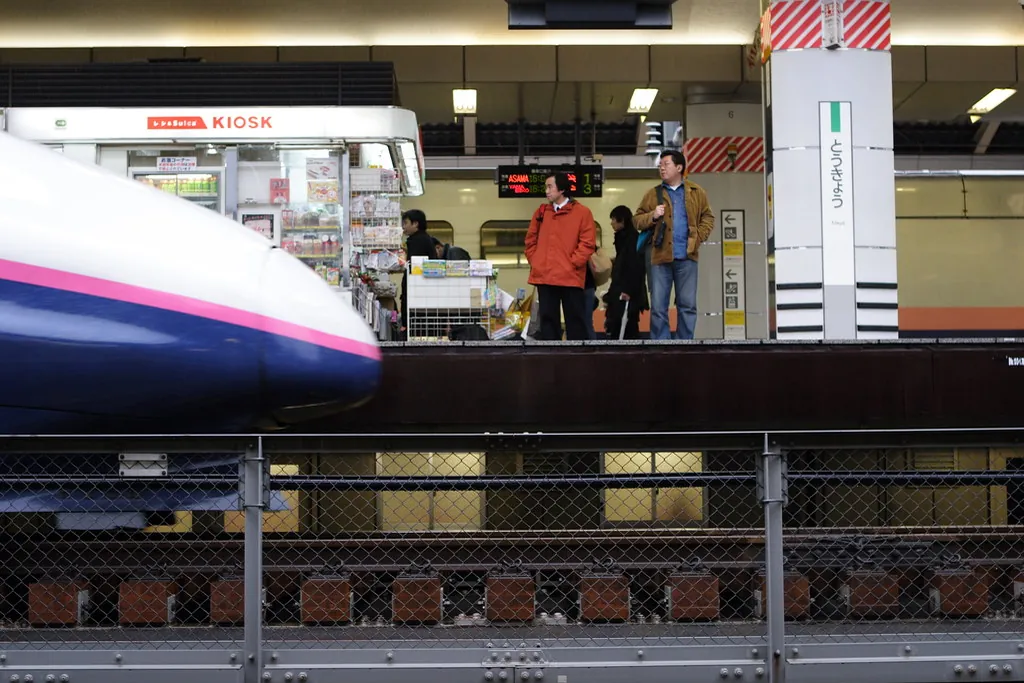 Shinkansen train stopped at a station platform next to a kiosk and waiting passengers