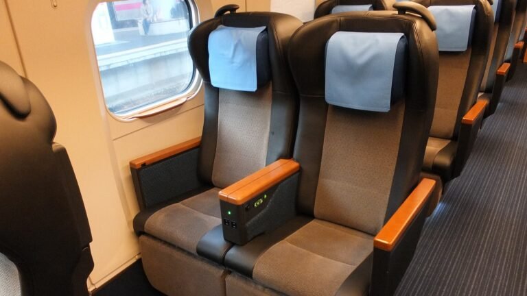 Grey Shinkansen Green Car seats with wood armrests and light blue headrest covers next to a window