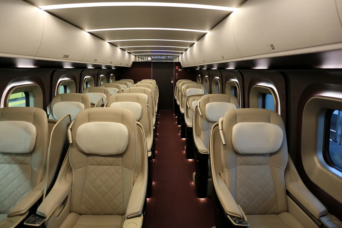 Rows of cream leather Gran Class seats with headrests inside a JR East E7 series Shinkansen car
