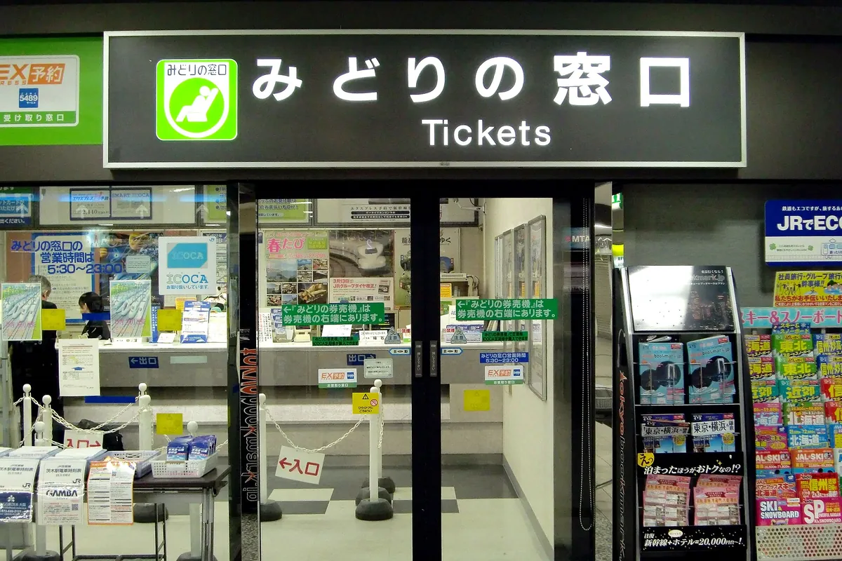 Entrance to a Midori no Madoguchi JR ticket office with a lit Tickets sign and brochure racks outside