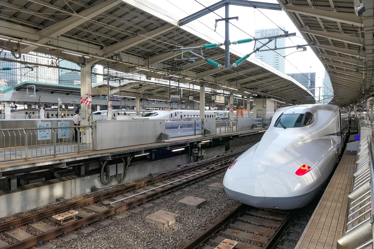 An N700 series Tokaido Shinkansen train at a Tokyo Station platform with other Shinkansen trains and city buildings behind