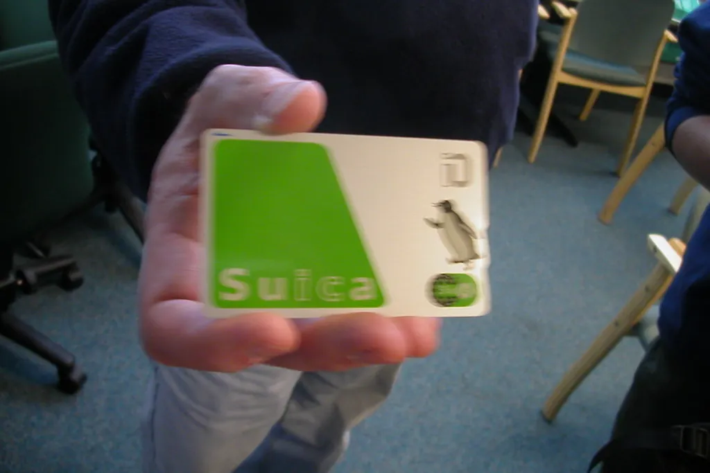 A hand holding a green Suica IC card with a penguin logo