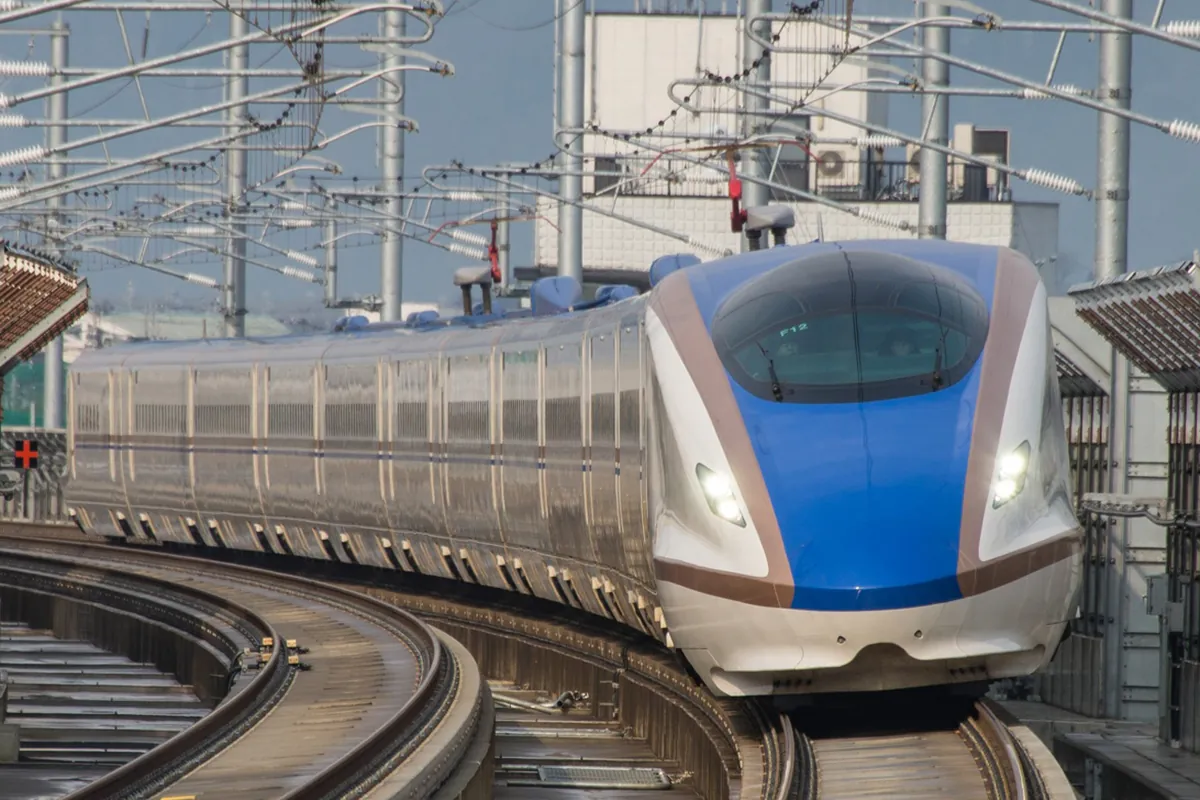 E7 series Hokuriku Shinkansen train approaching Shin-Takaoka Station on elevated tracks with overhead power lines