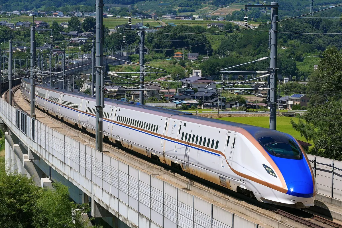 W7 series Hokuriku Shinkansen train running along an elevated viaduct through green countryside