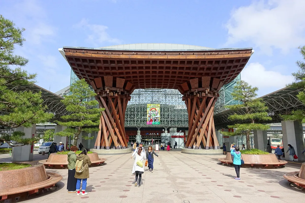 Wooden Tsuzumi Gate structure in front of Kanazawa Station with people walking through the plaza