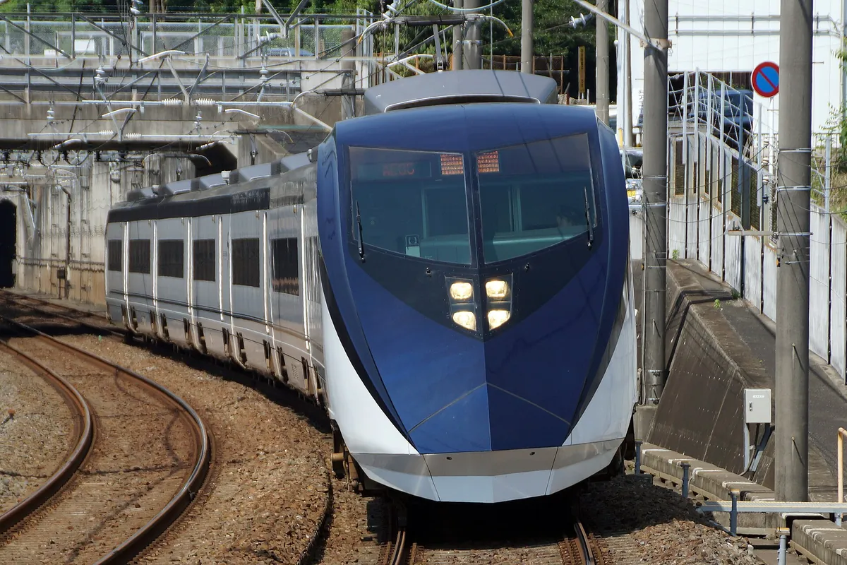 A navy-blue and white Keisei AE series Skyliner train curving along a track near station structures