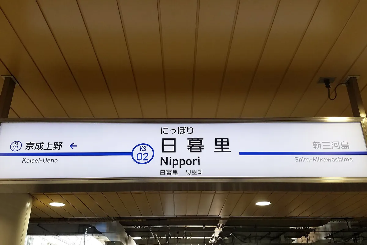 A station sign reading Nippori on the Keisei Main Line, shown in Japanese, English and Korean