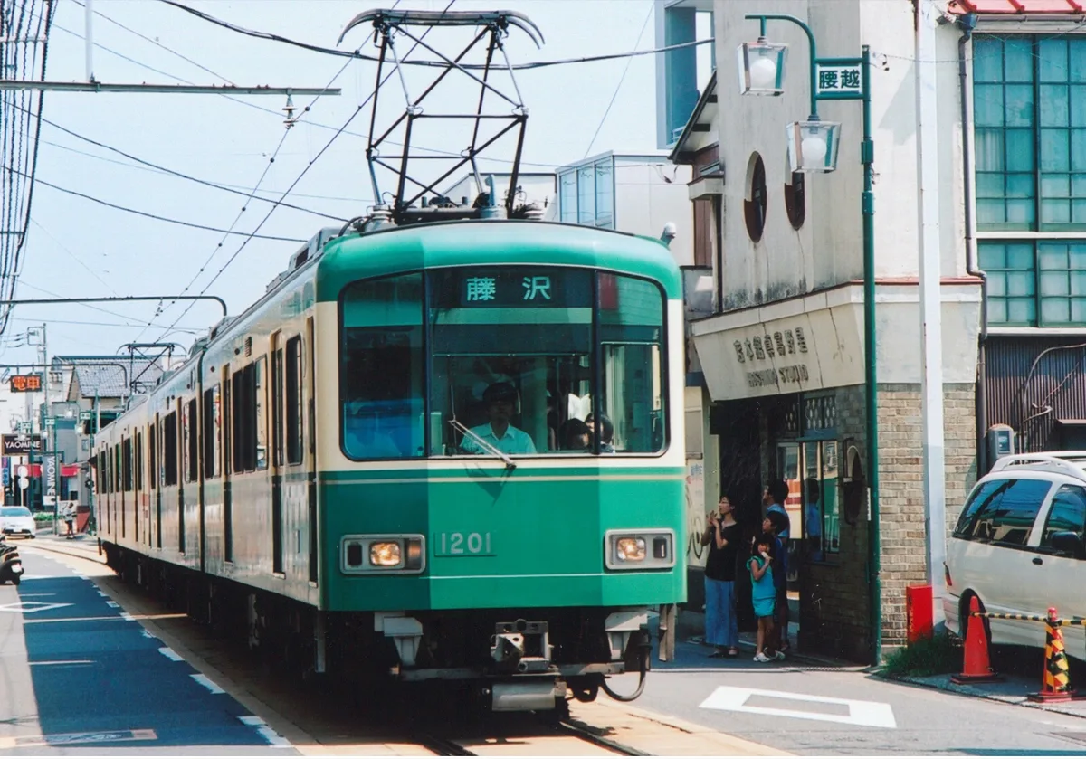 An Enoden train running down a narrow street between houses and shops in Kamakura, in 2026