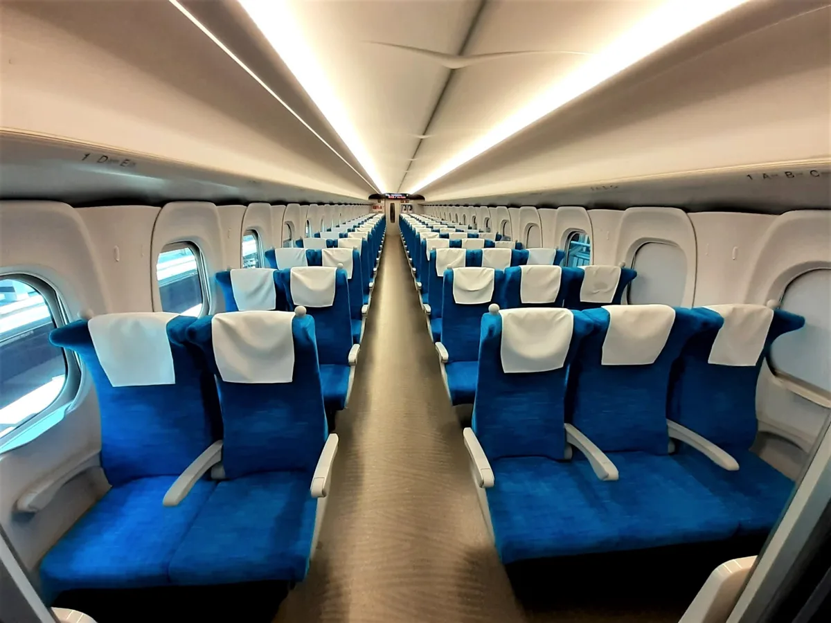 Ordinary car interior of a Shinkansen N700S, with blue seats in rows of two and three, in 2021